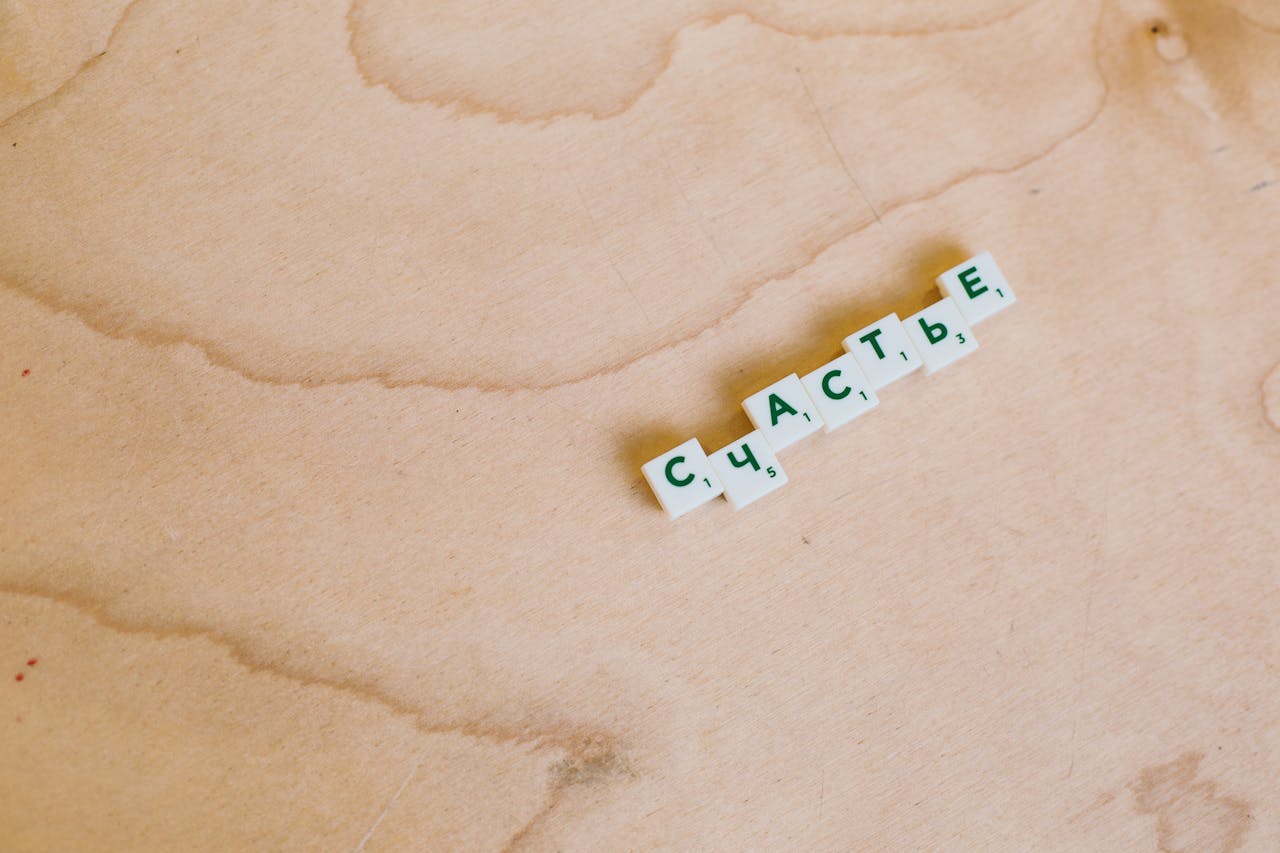 Cyrillic Scrabble tiles spelling 'happiness' on a wooden board.
